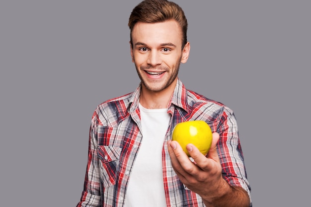 Gezond alternatief. Glimlachende man die groene appel voor zich houdt terwijl hij tegen een grijze achtergrond staat