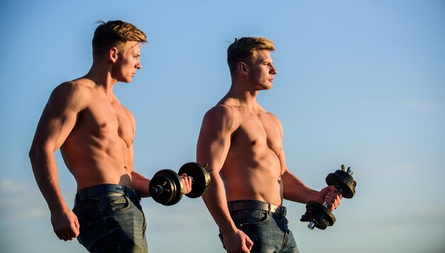 Gezond atletisch lichaam. Sexy torso aantrekkelijk lichaam. Mannelijkheid concept. Dubbele kracht. Gespierde tweeling. Mannen broers gespierde jongens hemelachtergrond. Sterke gespierde atleet bodybuilder. Aantrekkelijke tweeling.