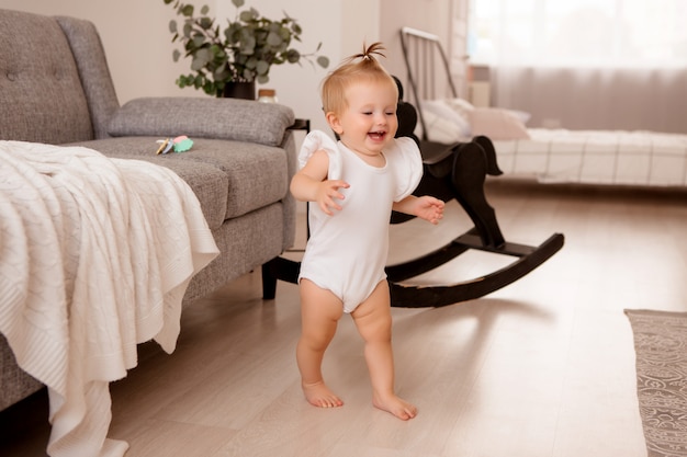 gezond babymeisje in een kamer naast een grijze bank leert lopen