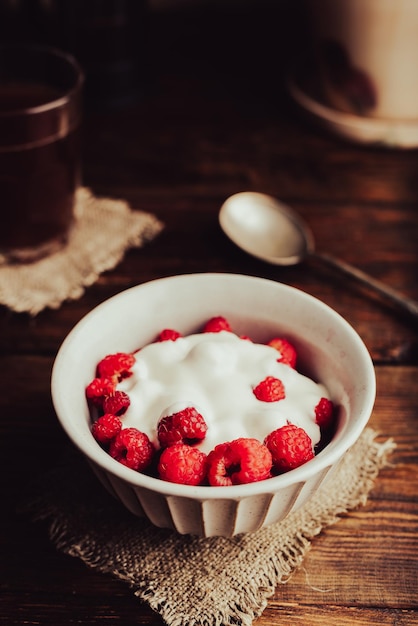 Gezond dessert met rijpe frambozen en room in een kom en een glas koffie op een rustieke tafel