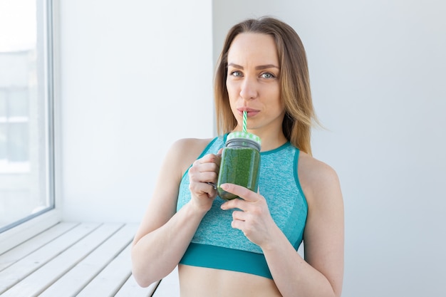 Gezond, dieet, detox en gewichtsverliesconcept - jonge vrouw in sportkleding met groene smoothie