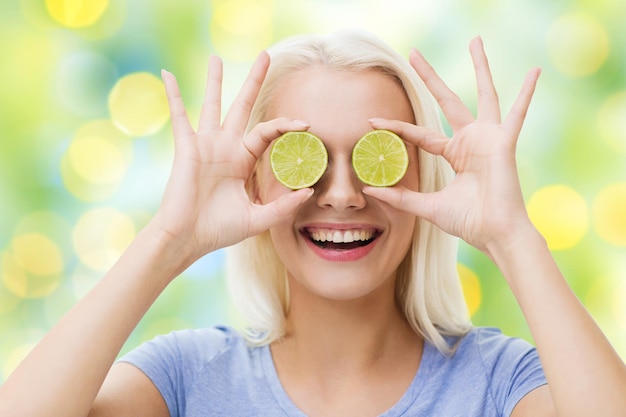 gezond eten, biologisch voedsel, fruitdieet, strip en mensenconcept - gelukkige vrouw die plezier heeft en haar ogen bedekt met limoenschijfjes over de zomer groene vakantie lichten achtergrond