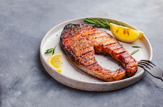 Gezond eten concept. gegrilde zalm steak met citroen, rozemarijn aangebraden op wit bord op grijze stenen achtergrond. flatlay met copyspace. omega-concept