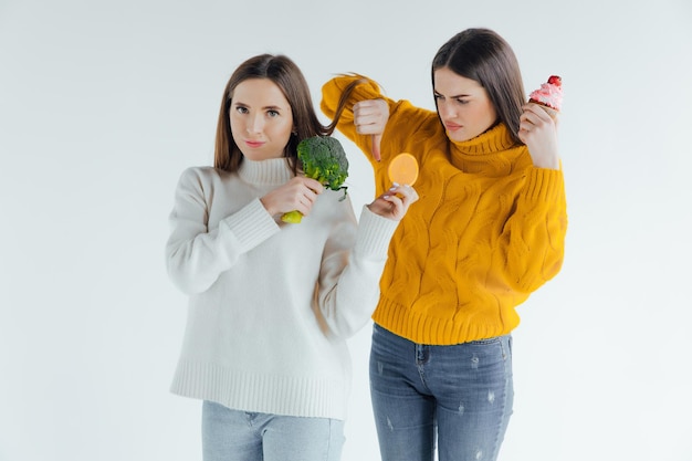 Gezond eten. De ene vrouw houdt broccoli vast en de andere een cake