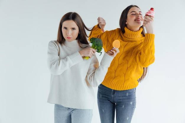 Gezond eten. De ene vrouw houdt broccoli vast en de andere een cake