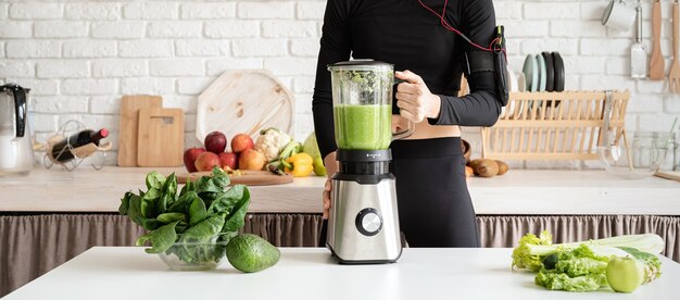 Gezond eten, dieet concept. Jonge blonde glimlachende vrouw die groene smoothie thuis keuken maakt