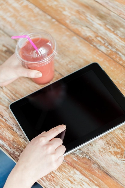 gezond eten, dieet, technologie en mensen concept - close-up van vrouw handen met kopje smoothie wijzende vinger naar tablet pc computer zwart leeg scherm op houten tafel