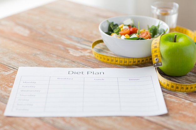 Foto gezond eten, diëten, afslanken en gewichtsverlies concept - close-up van dieetplan papier groene appel, meetlint en salade