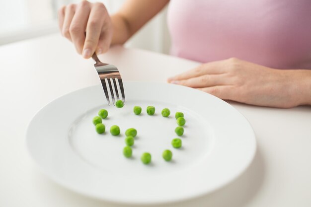 gezond eten, diëten, vegetarisch eten en mensen concept - close-up van een vrouw met een vork die erwten eet in de vorm van een hart