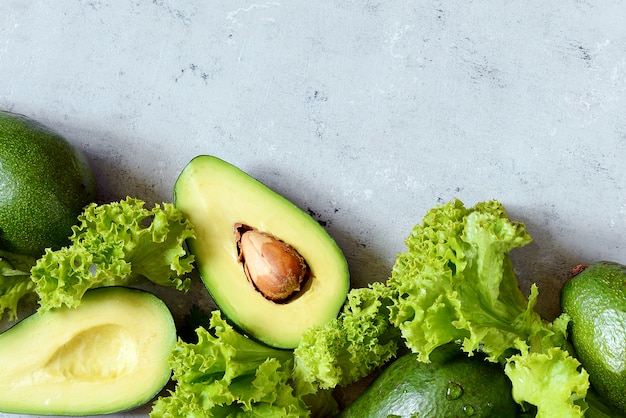 Gezond eten. Een halve rijpe avocado met zaad en sla op een plaat op een grijze muur.