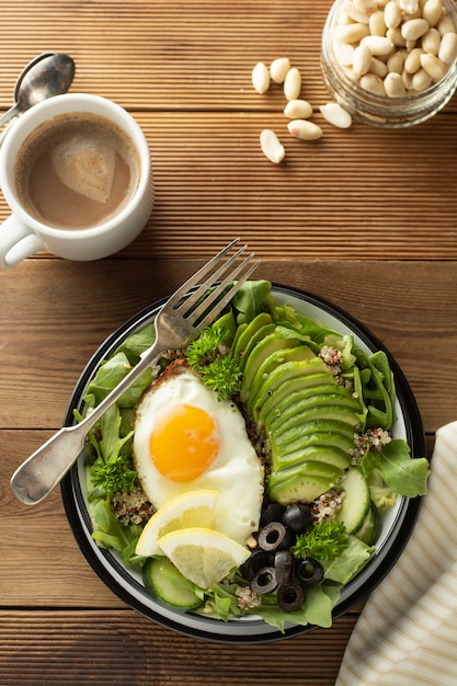 Gezond eten. Eieren, quinoa, avocado, groene salade, zwarte olijven. Houten tafel. dieet, afvallen.