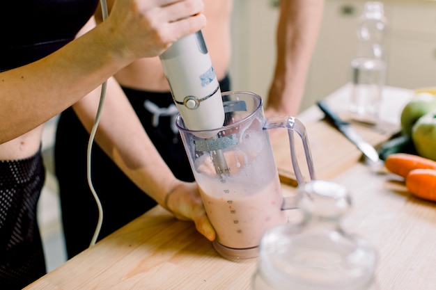 Gezond eten, fitnesslevensstijl, goede voeding. close-upfoto van mooie sportvrouw en man die gezonde smoothie maken. vrouw gebruikt handmixer