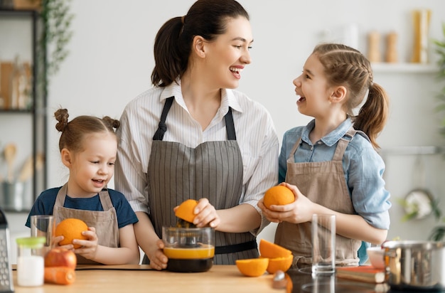 Gezond eten in huis. Gelukkige familie in de keuken. Moeder en kinderen dochters bereiden vers sinaasappelsap.