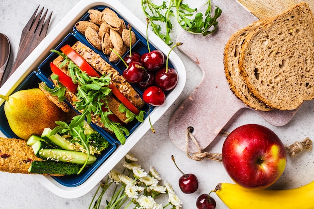 Gezond eten koken in lunchpakket. Sandwich, fruit, snacks op grijs