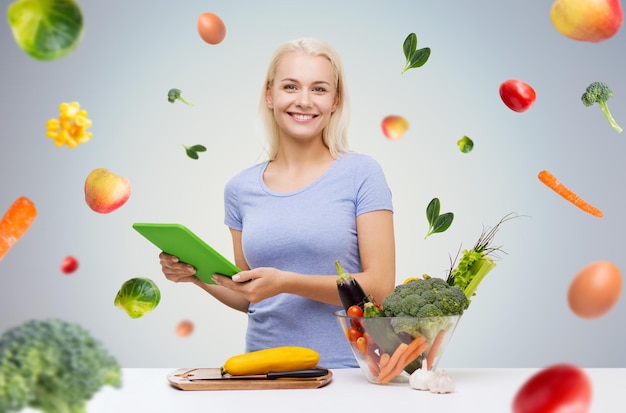 gezond eten, koken, vegetarisch eten, technologie en mensen concept - lachende jonge vrouw met tablet pc-computer en kom groenten over grijze achtergrond met vallende groenten