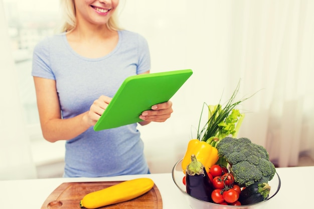 gezond eten, koken, vegetarisch eten, technologie en mensenconcept - close-up van lachende jonge vrouw met tablet pc-computer en kom groenten thuis