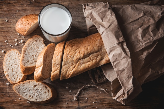 Gezond eten. Lang landbrood met twee afgesneden stukken ligt op een houten snijplank en een glas verse melk.