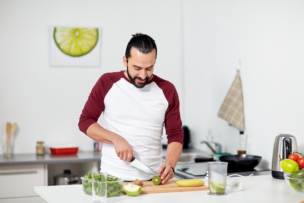 gezond eten, vegetarisch eten, dieet en mensenconcept - gelukkige jonge man met blender en fruit koken thuis keuken