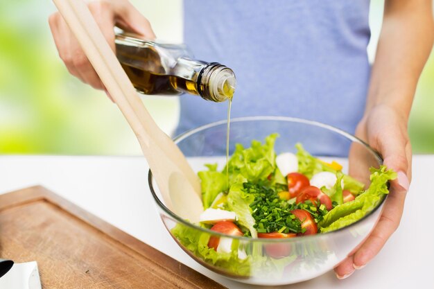 gezond eten, vegetarisch eten, diëten en mensenconcept - close-up van jonge vrouw die groentesalade met olijfolie kleedt over groene natuurlijke achtergrond