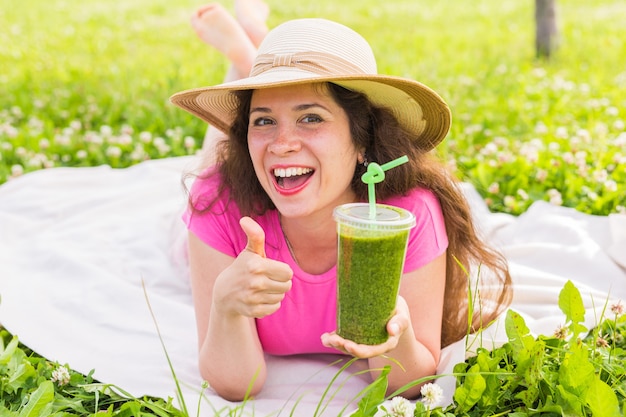 Gezond eten, zomer en mensen concept - Jonge vrouw heeft plezier in het park en drink groene smoothies tijdens een picknick