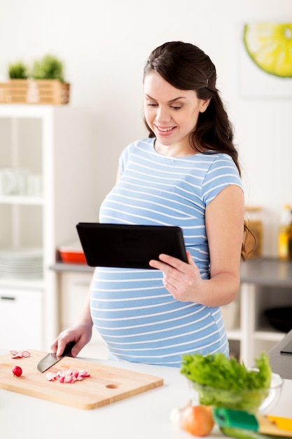 gezond eten, zwangerschap en mensenconcept - zwangere vrouw met tablet pc-computer koken groentesalade thuis keuken