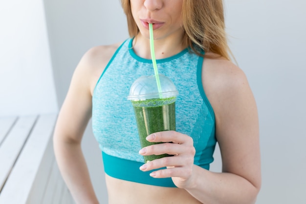 Gezond, fitness en detox concept - close-up van jonge vrouw in sportkleding met groene smoothie binnenshuis