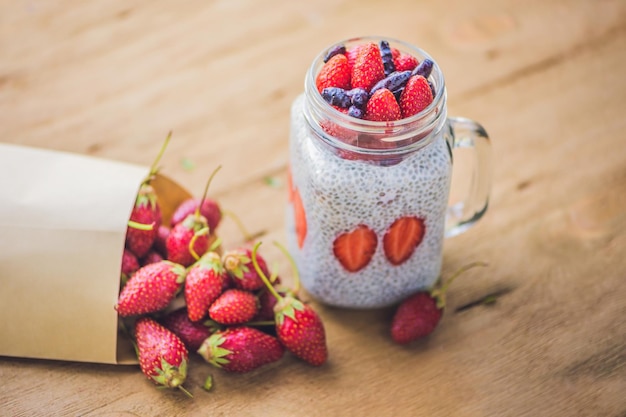 Gezond gelaagd dessert met chia pudding, aardbei en kamperfoelie in een glazen pot op rustieke achtergrond.