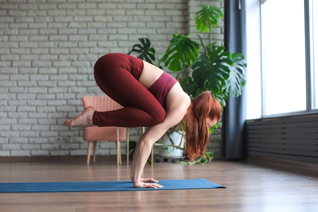 Gezond leven. Aantrekkelijke vrouw die thuis yoga beoefent, aan het trainen is, sportkleding draagt.