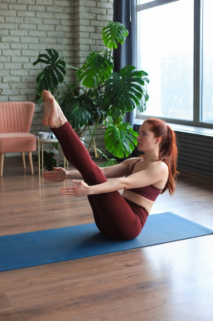 Gezond leven. Aantrekkelijke vrouw die thuis yoga beoefent, aan het trainen is, sportkleding draagt.