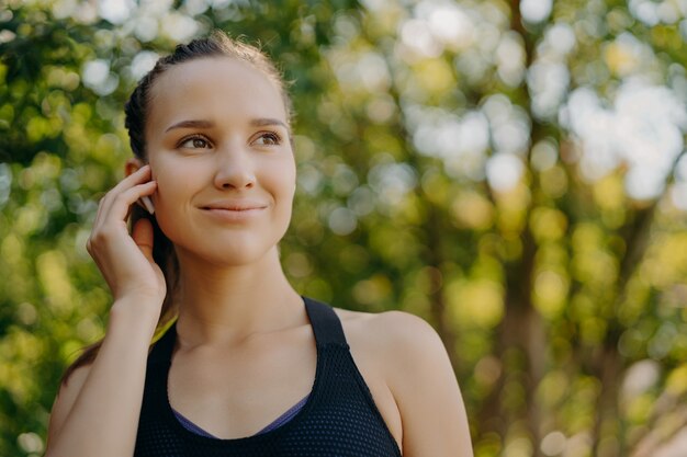 Gezond levensstijlconcept. Buitenopname van sportvrouw geniet van favoriete afspeellijst in oordopjes tijdens het trainen in het park