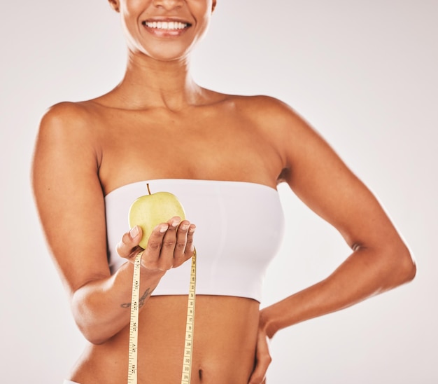 Gezond meetlint en lichaam met zwarte vrouw en appel voor voeding en dieet met fitness geïsoleerd op studio achtergrond Wellness glimlach en gezondheid levensstijl met gewichtsverlies en schoon eten
