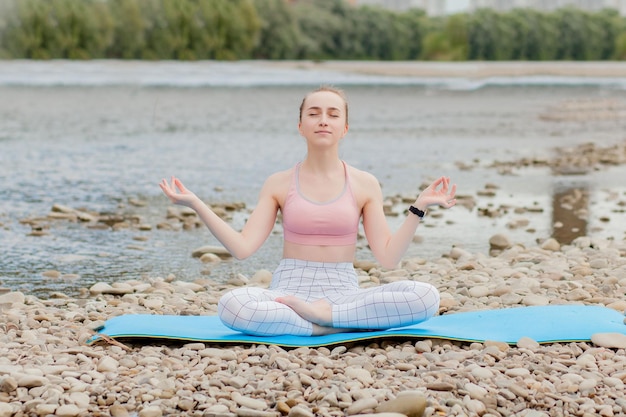 Gezond meisje ontspannen tijdens het mediteren en het doen van yoga-oefening in de prachtige natuur aan de oever van de rivier