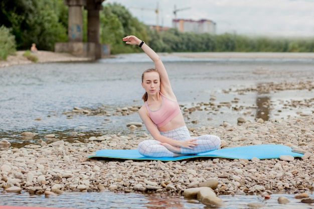 Gezond meisje ontspannen tijdens het mediteren en het doen van yoga-oefeningen in de prachtige natuur aan de oever van de rivier.