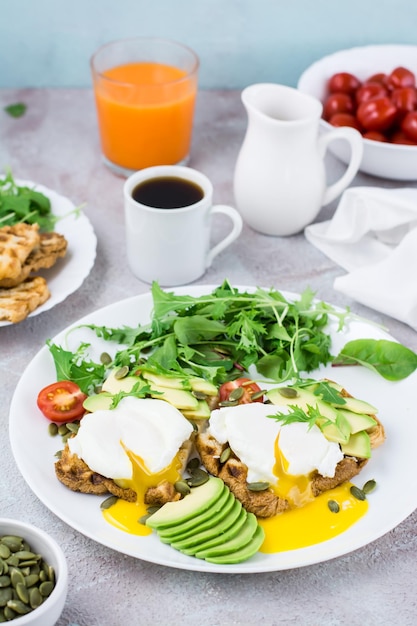 Gezond ontbijt. Gepocheerde eieren op toast met avocado stukjes, rucola, mizuna en snijbiet bladeren en cherrytomaatjes op een bord op een geserveerd tafel. Flexetariër dieet. Verticale weergave