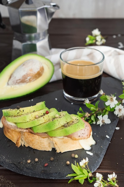 Gezond ontbijt. Geroosterd granenbrood met vers gesneden avocado, ham, kaas en kopje koffie