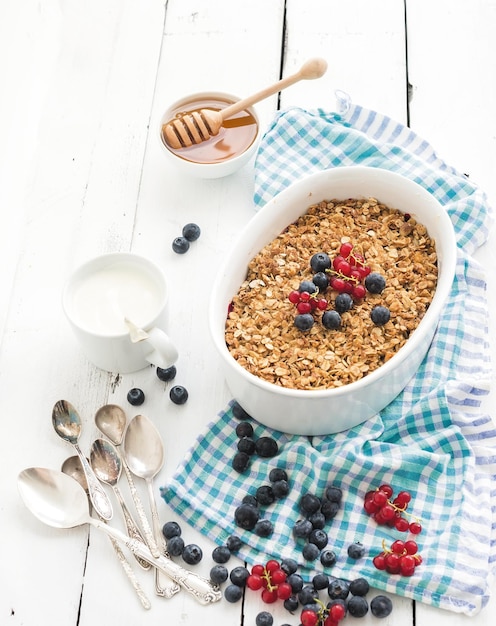 Foto gezond ontbijt haver muesli bessen crumble met verse bosbessen yoghurt en honing in keramische ovenschaal over witte rustieke achtergrond