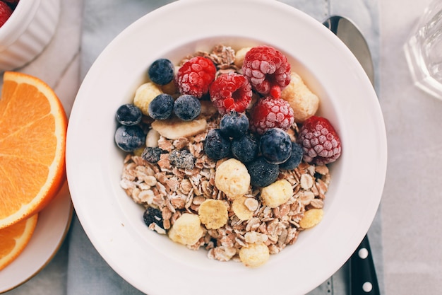 Gezond ontbijt: havermout met frambozen, sinaasappels en bosbessen. Zelfgemaakte Granola. Gezonde ontbijtingrediënten. Kom havergranola met melk, vers fruit. Bovenaanzicht, kopie ruimte