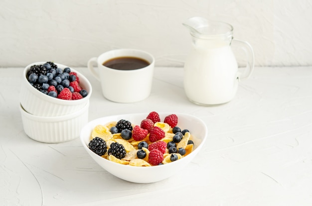 Gezond ontbijt met cornflakes, frambozen, bramen, bosbessen, melk en koffie op een witte ondergrond