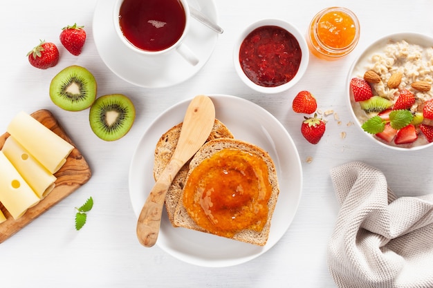 Gezond ontbijt met havermoutpap, aardbei, noten, toast, jam en thee. Bovenaanzicht