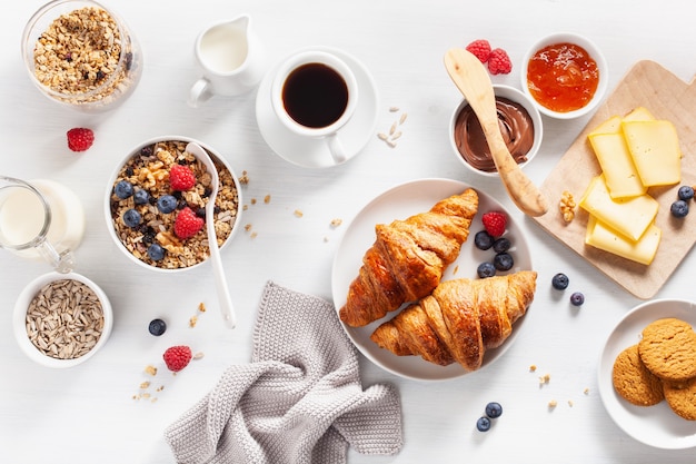 Gezond ontbijt met muesli, bessen, noten, croissants, jam, chocopasta en koffie. bovenaanzicht