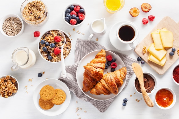Gezond ontbijt met muesli, bessen, noten, croissants, jam, chocopasta en koffie. Bovenaanzicht