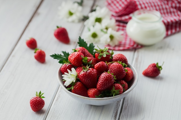 Gezond ontbijt met rijpe zoete bessen en zuivelproduct. Verse aardbeien in keramische kom en natuurlijke bio yoghurt op witte rustieke houten tafel