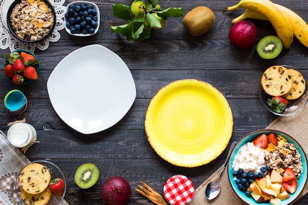 Gezond ontbijt, ontbijtgranen met yoghurt, aardbeien, bosbessen, appel, banaan, op rustieke houten. Bovenaanzicht