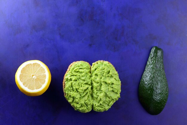 Gezond ontbijt toast met avocado smash Toast en een halve avocado met een schil en gele citroen op een blauwe achtergrond Closeup Vegetarisch eten concept