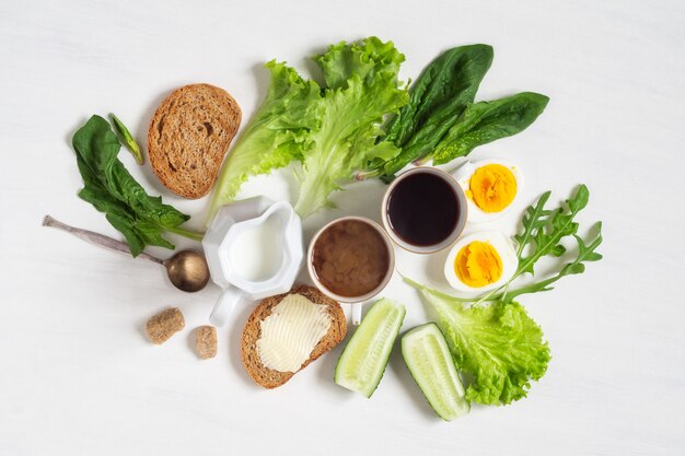 Gezond ontbijt. Twee kopjes koffie met gehalveerde gekookte eieren, toast met boter en spinazieblaadjes en salade op een witte tafel