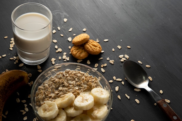 Gezond ontbijt van havermout met banaan, een glas melk en wat koekjes op de zwarte tafel