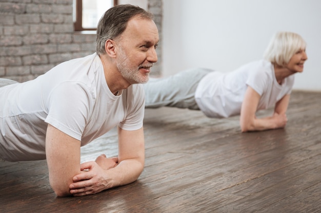 Gezond pensioneringspaar dat positief is terwijl het doen van yogahoudingen op hun tutor kijken