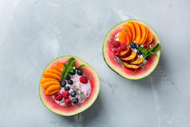 Gezond schoon eten dieet en voeding seizoensgebonden zomer ontbijt concept Fruitsalade met yoghurt in gesneden watermeloen kom op een keukentafel Bovenaanzicht plat lag kopie ruimte achtergrond