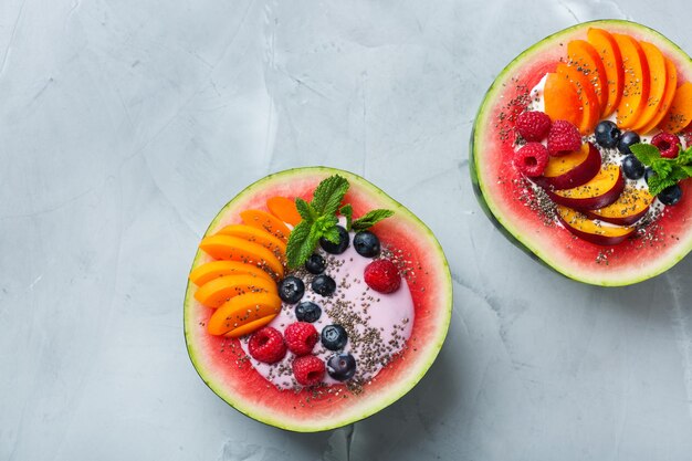 Gezond schoon eten dieet en voeding seizoensgebonden zomer ontbijt concept Fruitsalade met yoghurt in gesneden watermeloen kom op een keukentafel Bovenaanzicht plat lag kopie ruimte achtergrond