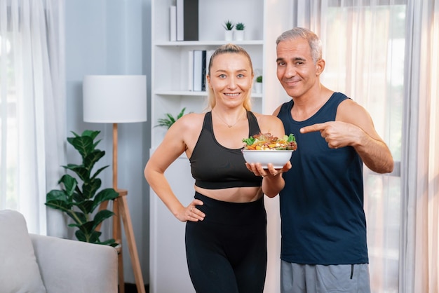 Gezond senior koppel in sportkleding met een kom fruit en groente Gezonde keukenvoeding en veganistische levensstijl voor fitness lichaamsbouw concept Slagkracht